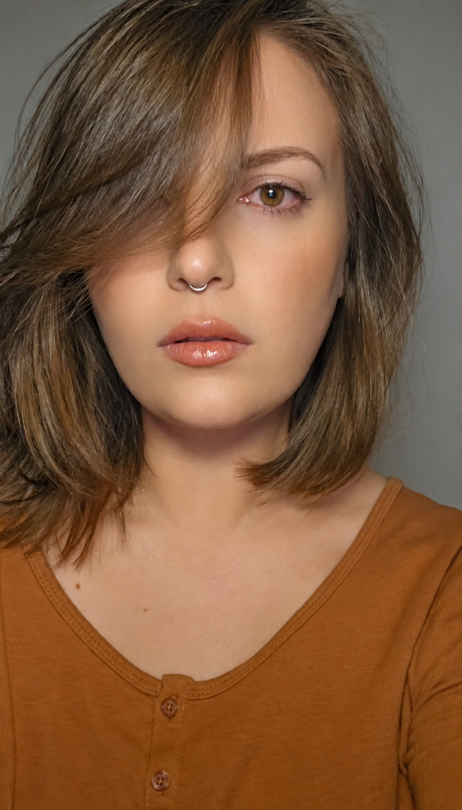Kasha with her hair falling across one eye, wearing a warm brown top